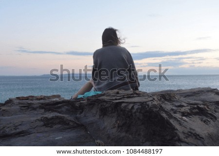 Back of a young women sitting on a rock and looking at the sunrise on the ocean - A little bite of the australian beauty