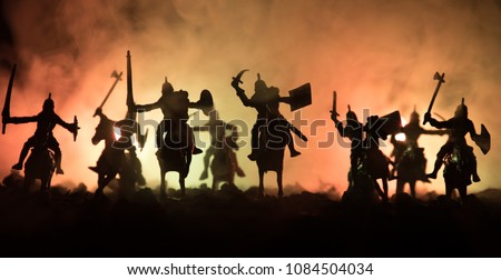 Medieval battle scene with cavalry and infantry. Silhouettes of figures as separate objects, fight between warriors on dark toned foggy background. Night scene. Selective focus Royalty-Free Stock Photo #1084504034