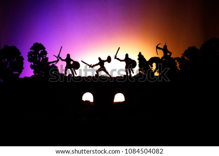 Medieval battle scene on bridge with cavalry and infantry. Silhouettes of figures as separate objects, fight between warriors on dark toned foggy background. Night scene. Selective focus