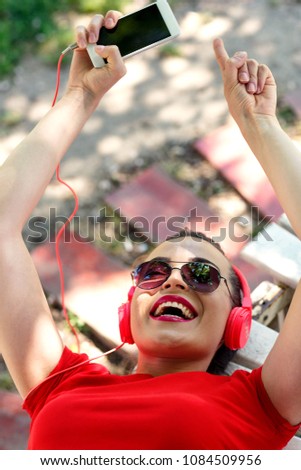 
young girl having fun listening to the music from a smartphone lying in a bench of a park
