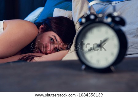 Image of brunette with insomnia lying on bed next to alarm clock at night