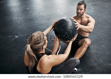 Two fit young people in sportswear sitting on a gym floor working out together with a medicine ball during an exercise session Royalty-Free Stock Photo #1084561529