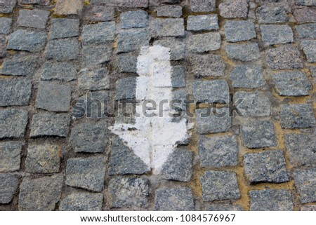 A downwards arrow painted with white paint on the old stoneblock pavement cobbled with square granite blocks
