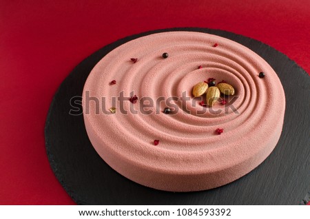 Chocolate mousse cake covered with Pink Velvet Cocoa Spray decorated with almond and chocolate balls on black board on red background