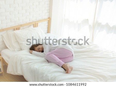 Beautiful womem sleeping in the bedroom. Asian lady sleep well.Sleeping in a white room makes you feel comfortable.Asian girl wearing pink pants, white coat curled In bed in a white room.Warm tone.