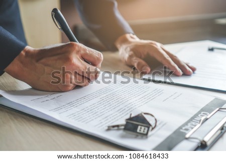 close-up view hands of businessman signing leasing home documents and have a apartment keys on paperwork.