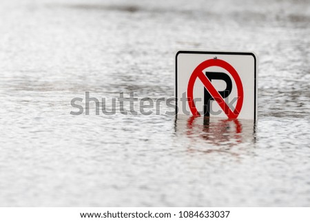 A No Parking sign in water. Water completely covers the signpost and partially covers the sign. Closeup view.