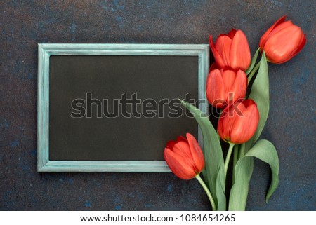 Blackboard and bunch of red tulips on abstract dark background, space for your test. Flat lay, toned image.