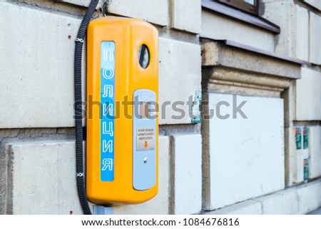 Public yellow emergency telephone, outdoor on building facade. Inscription in Russian - police
