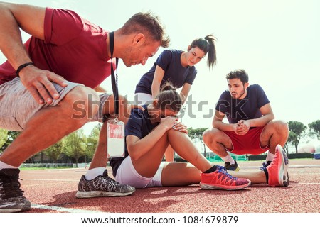young athlete injured to knee on the track while being helped by his coach and his teammates Royalty-Free Stock Photo #1084679879