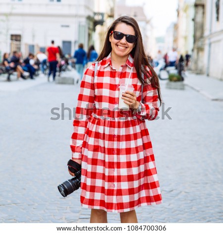 woman walking by city streets with cool drink and camera
