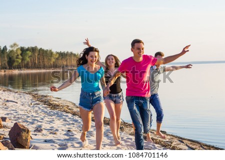 Friends are running along the seashore, holding hands and laughing. Young people, boys and girls, students are happy on the beach