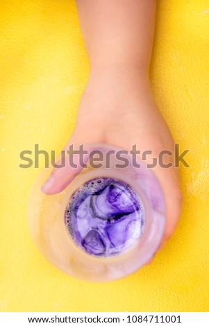 Child's hand with a glass of paint on top.