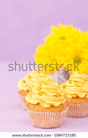 Cupcakes decorated with yellow cream and chrysanthemums on violet pastel background. Closeup photography of sweet baked dessert in minimalism concept.