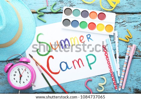 Inscription Summer Camp with alarm clock and pens on wooden table