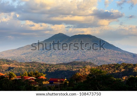 CATARINA, NICARAGUA: View of volcano Mombacho from Catarin mirador. Village buildings in foreground. Royalty-Free Stock Photo #108473750