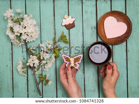 Woman hands holding a cup of coffee on chabby chic wooden table.  Cherry blossom  flowers and ginger biscuits. Mothers day or valentines day background concept.