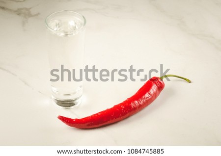 shot of vodka and red hot chili pepper on the bar/shot of vodka and red hot chili pepper on a white marble background. Selective focus