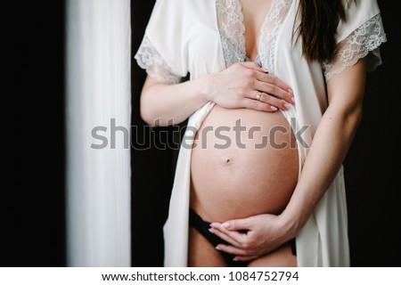 Waiting baby. Pregnant woman standing and hands embraces a round belly, stomach. close-up. nine months. Baby Shower. Motherhood concept. front view.