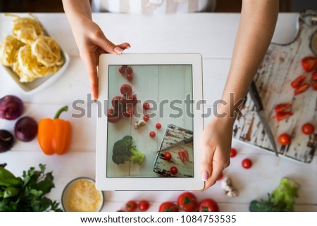 Hands with  tablet computer close-up pictures of food. Various fresh Ingredients for cooking tasty vegetarian lunch from fresh vegetables. Sliced vegetables prepared for making meal. Selective focus.