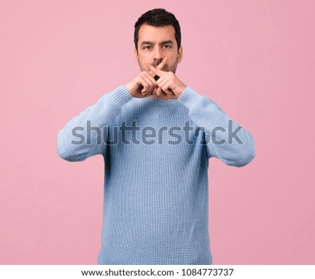 Handsome man showing a sign of closing mouth and silence gesture on pink background