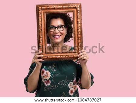 Middle aged woman smiling and relaxed, looking through a frame, funny and creative photo, concept of photography