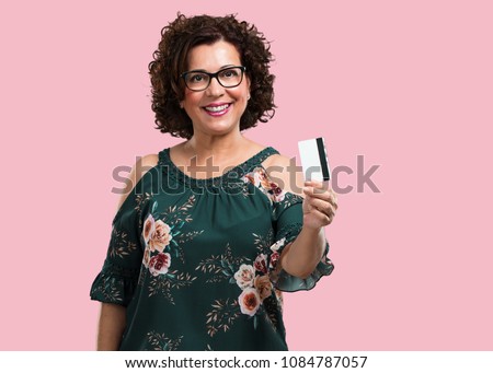Middle aged woman cheerful and smiling, very excited holding the new bank card, ready to go shopping