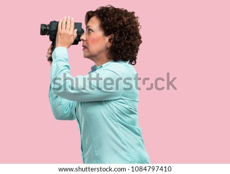 Middle aged woman excited and entertained, looking through a film camera, looking for an interesting shot, recording a movie, executive producer