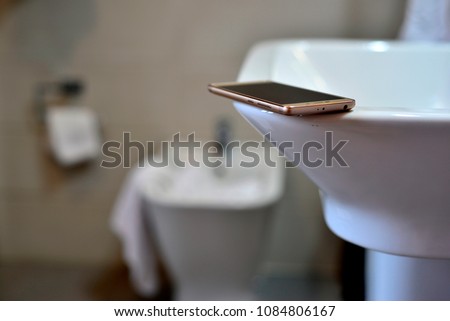 mobile phone on white washbasin and bidet defocused in the background