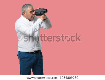 Middle aged man excited and entertained, looking through a film camera, looking for an interesting shot, recording a movie, executive producer