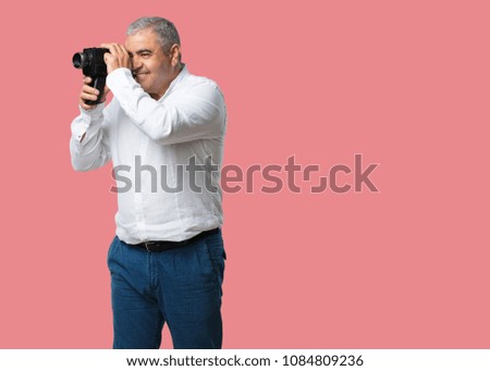 Middle aged man excited and entertained, looking through a film camera, looking for an interesting shot, recording a movie, executive producer