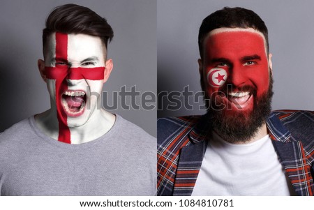Emotional soccer fans with painted England and Tunisia flags on faces. Confrontation of football team supporters from rival countries, sport event, faceart and patriotism concept. Royalty-Free Stock Photo #1084810781