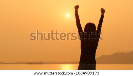 Woman raising hand up under sunset 