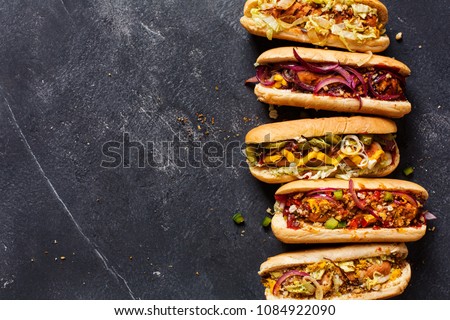 Hot dogs with different toppings on a dark background. Food background with copy space, top view. Fast food. Royalty-Free Stock Photo #1084922090