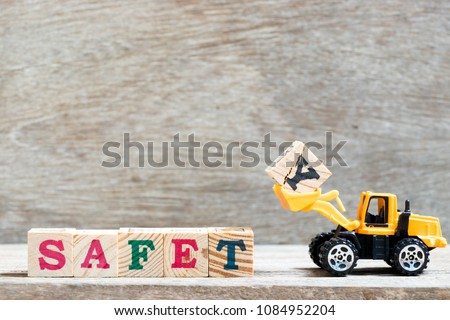 Toy bulldozer hold letter block y to complete word safety on wood background