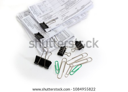 Various binder clips and wire paper clips different sizes and documents with blurred text binded using these clips on a white background
