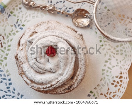 Close up of muffin dessert decorated with sugar powder. Fresh cruffin upon white doily with spoon and sieve. Selective focus.