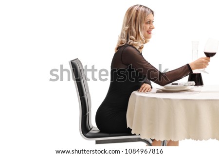Young woman seated at a restaurant table holding a glass of red wine isolated on white background