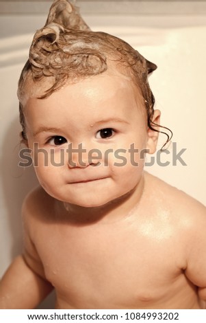 One small beautiful male child with wet hair sitting in bathroom smiling looking forward on white background, vertical picture