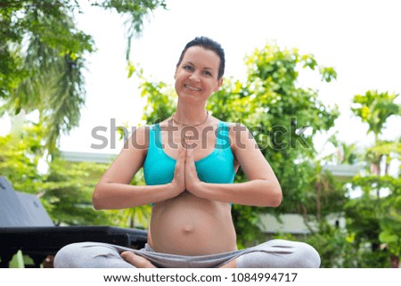 A pregnant woman is meditating near the pool. Yoga. The lotus position.