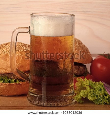 Few fresh tasty burgers of green lettuce meat cutlet tomato and white bun with sesame seeds near and glass of light beer with froth on octoberfest holiday on wooden background, square picture