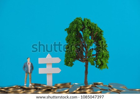 Figure miniature businessman or small people investor standing on coin stack with white wooden board sign and little tree decoration, for money and financial business success concept idea.