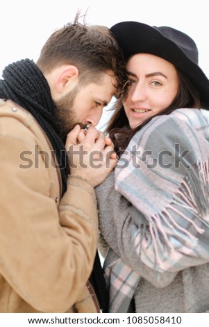 Portrait of caucasian man with beard holding woman hand in white background, wearing coat with scarf. Concept of couple seasonal winter photo session and romantic feelings.