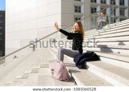 Girl sitting on stairs and making selfie by smartphone. Concept of modern technology and European youth, front facing camera..