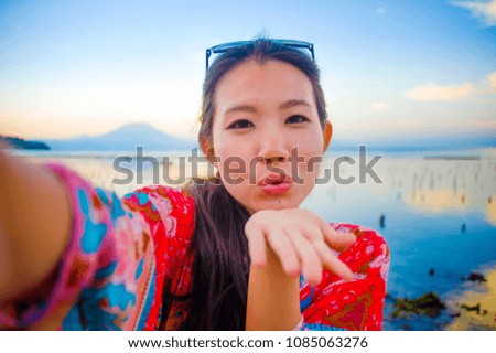 self portrait of gorgeous beautiful and happy Asian Korean or Chinese woman 20s taking selfie photo with mobile phone camera in exotic tropical beach enjoying summer holidays trip smiling cheerful