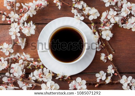 Sakura branches with flowers around White cup with black coffee in the center of the picture on a dark wooden background. Flat lay, top view.