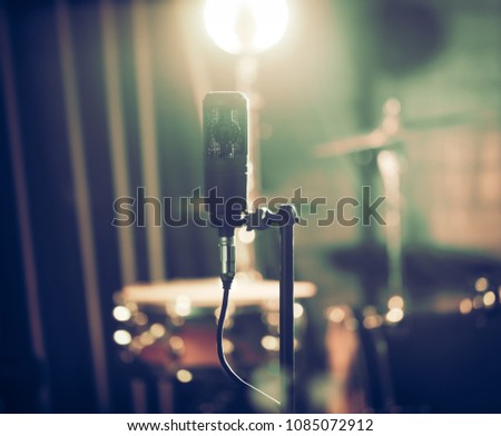 Microphone in recording Studio or concert hall close-up, with drum set on background out of focus. Beautiful blurred background of colored lanterns. Musical concept in vintage style.