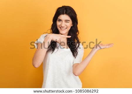 Photo of happy cute young pretty woman pointing standing isolated over yellow background.