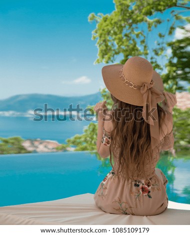 Beautiful Fashion Woman in beach hat enjoying sea view by swimming pool on luxury tropical resort. Exotic Paradise. Travel, Tourism and Vacations Concept. Elegant lady.