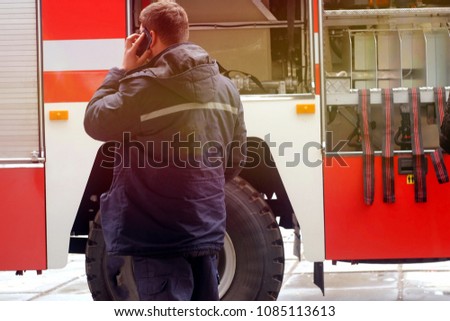 a man with a phone in his hands talking near a red fire engine with fire fighting equipment

